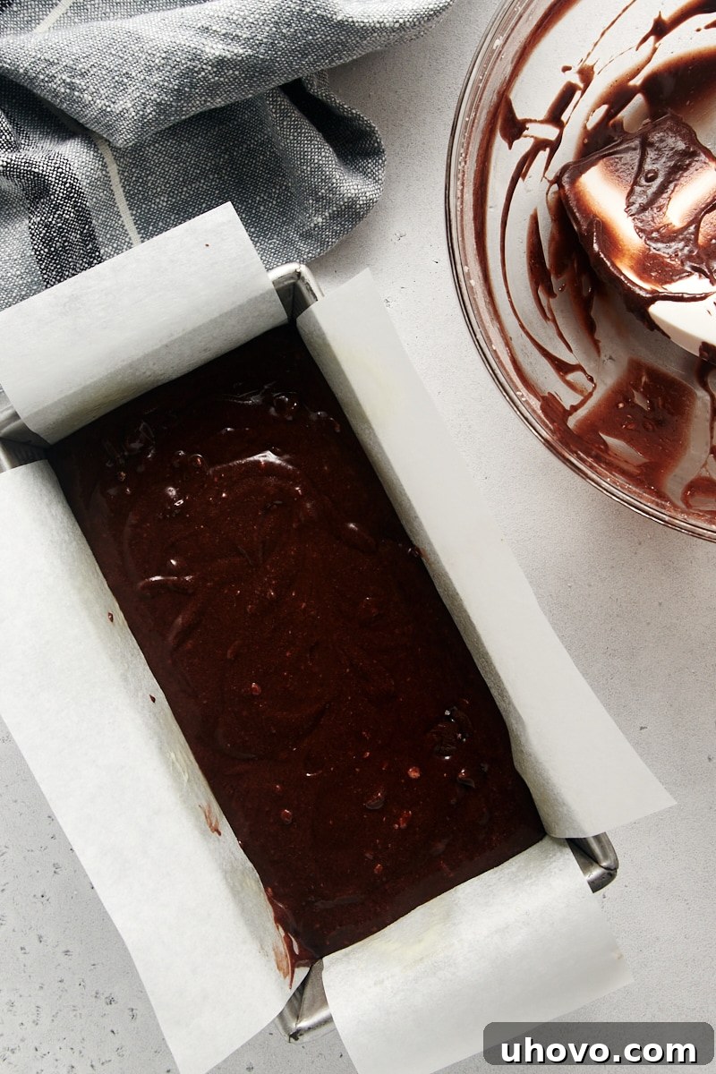 An overhead view of the smooth Chocolate Loaf Cake batter, meticulously spread in a parchment-lined loaf pan, poised for baking.