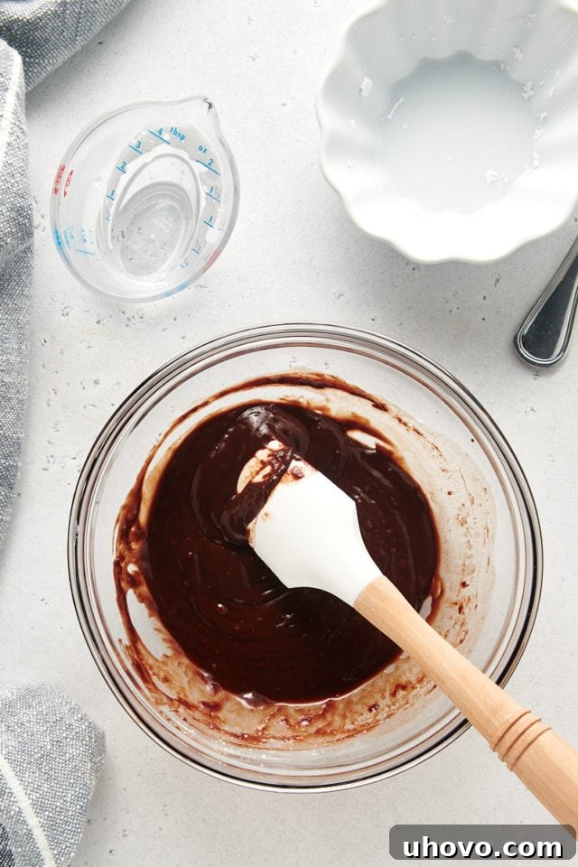 A close-up, overhead shot of the perfectly mixed chocolate glaze in a transparent glass bowl, showcasing its smooth, glossy, and pourable consistency.