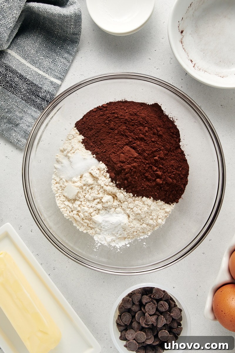 An overhead shot of dry ingredients for the Chocolate Loaf Cake, including flour and cocoa powder, in a clear glass mixing bowl, ready to be combined.