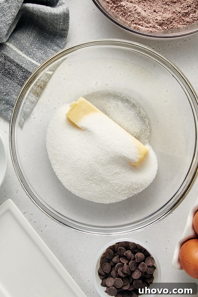 An overhead perspective of granulated sugar and softened butter, perfectly creamed together in a clear glass mixing bowl, forming the base of the wet ingredients.
