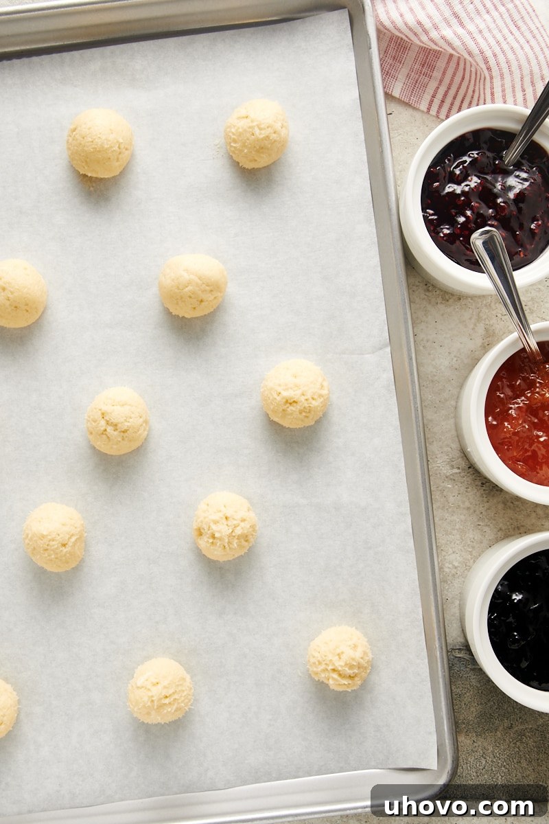 Neatly rolled balls of Cream Cheese Thumbprint Cookie dough arranged on a parchment-lined baking sheet, ready for indentation.