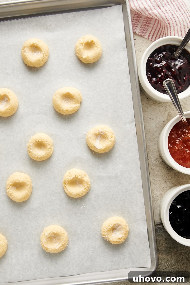 Cream Cheese Thumbprint Cookie dough balls on a baking sheet, each with a distinct indentation made in the center, ready for jam filling.