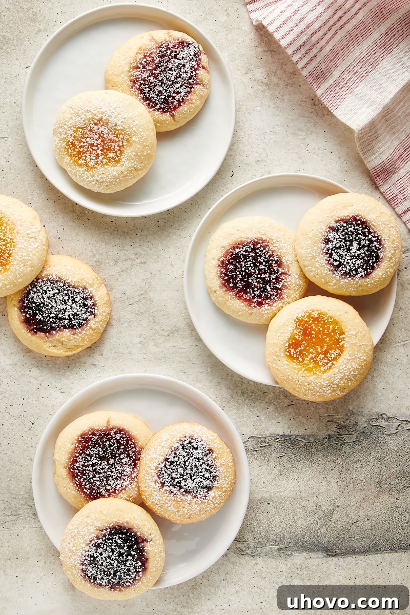 Cream Cheese Thumbprint Cookies arranged on white plates, showcasing the variety of vibrant jam fillings in their perfectly formed centers.