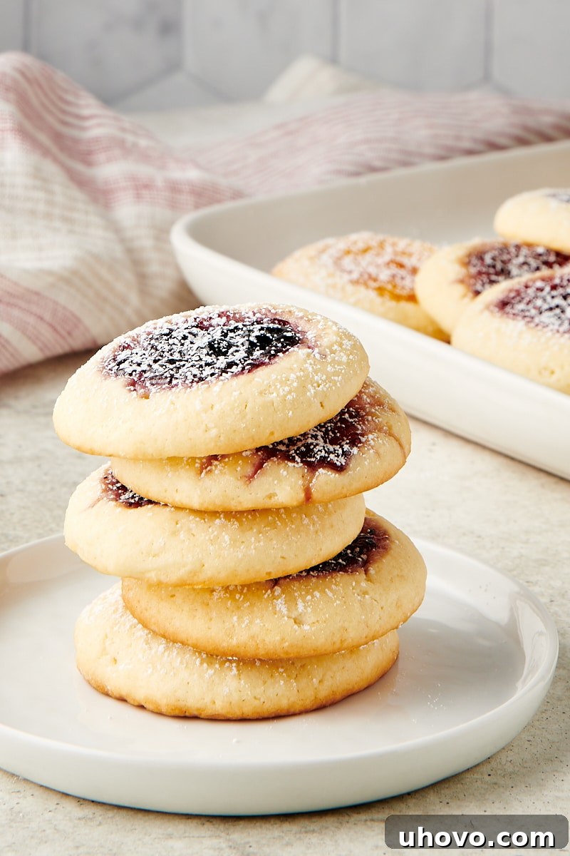 A perfectly stacked tower of Cream Cheese Thumbprint Cookies on a white plate, showcasing their inviting jam centers and soft texture.