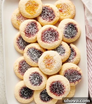 Overhead view of glistening jam-filled Cream Cheese Thumbprint Cookies arranged neatly on a white tray, showcasing their vibrant colors and perfect indentations.