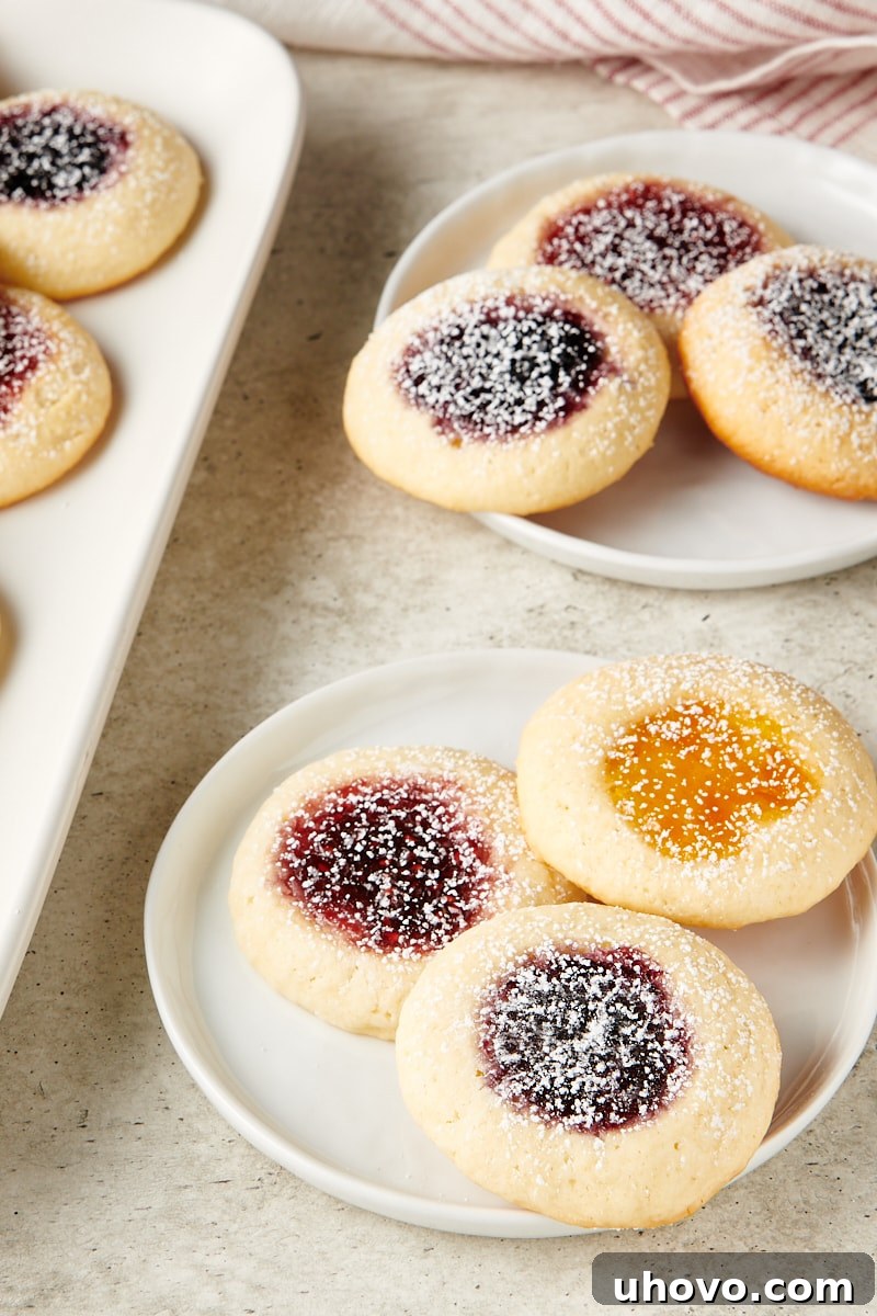 A collection of Cream Cheese Thumbprint Cookies artfully arranged on white plates, highlighting the various jam fillings and delicate texture.