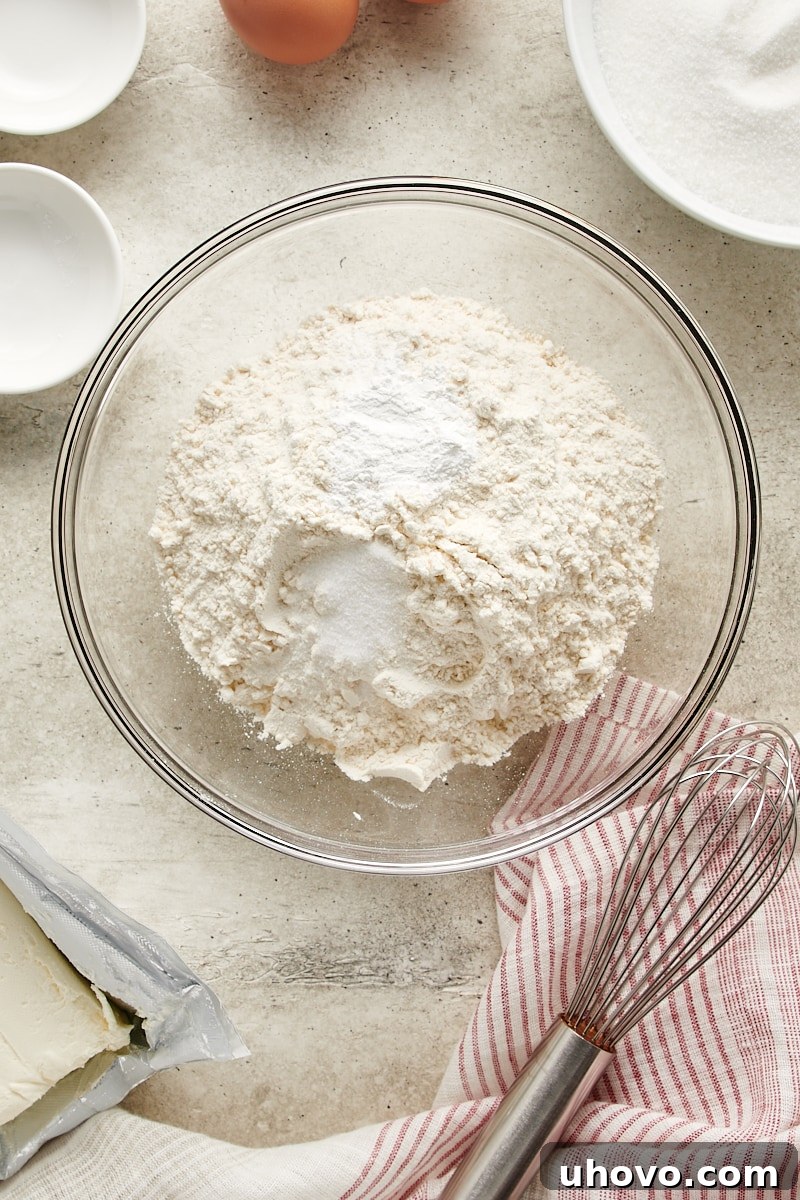 Overhead view of all-purpose flour, baking powder, and salt measured in a clear glass mixing bowl, ready to be whisked together.