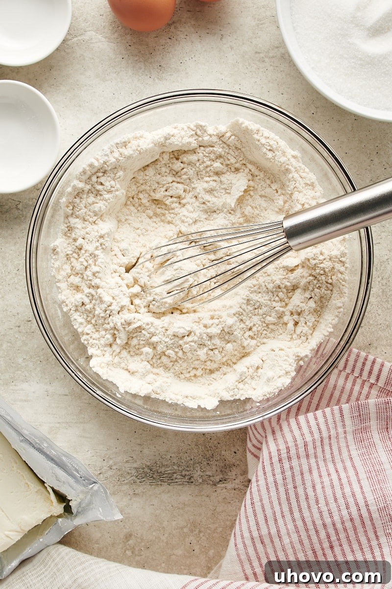 Overhead view of the well-combined dry ingredients for Cream Cheese Thumbprint Cookies, showing a uniform blend of flour, baking powder, and salt in a glass bowl.