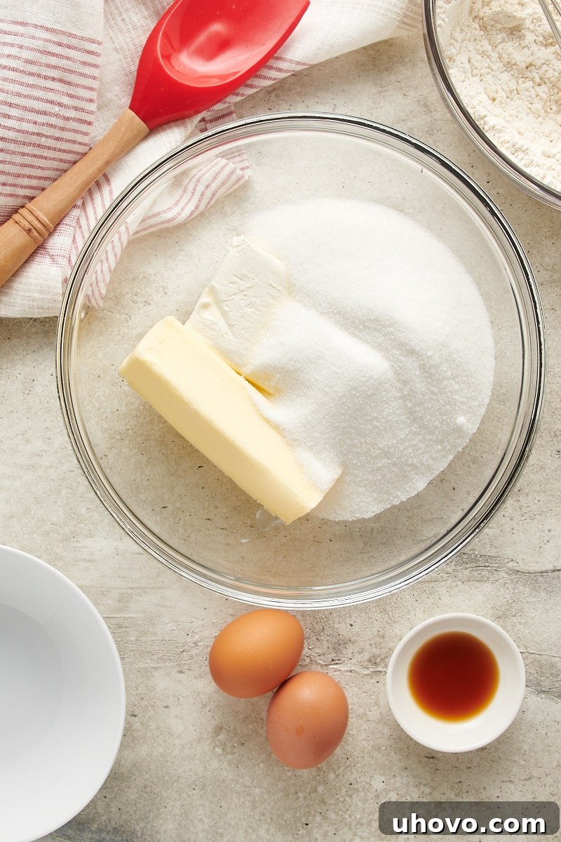 Overhead view of softened butter, cream cheese, and granulated sugar in a glass mixing bowl, poised for creaming.