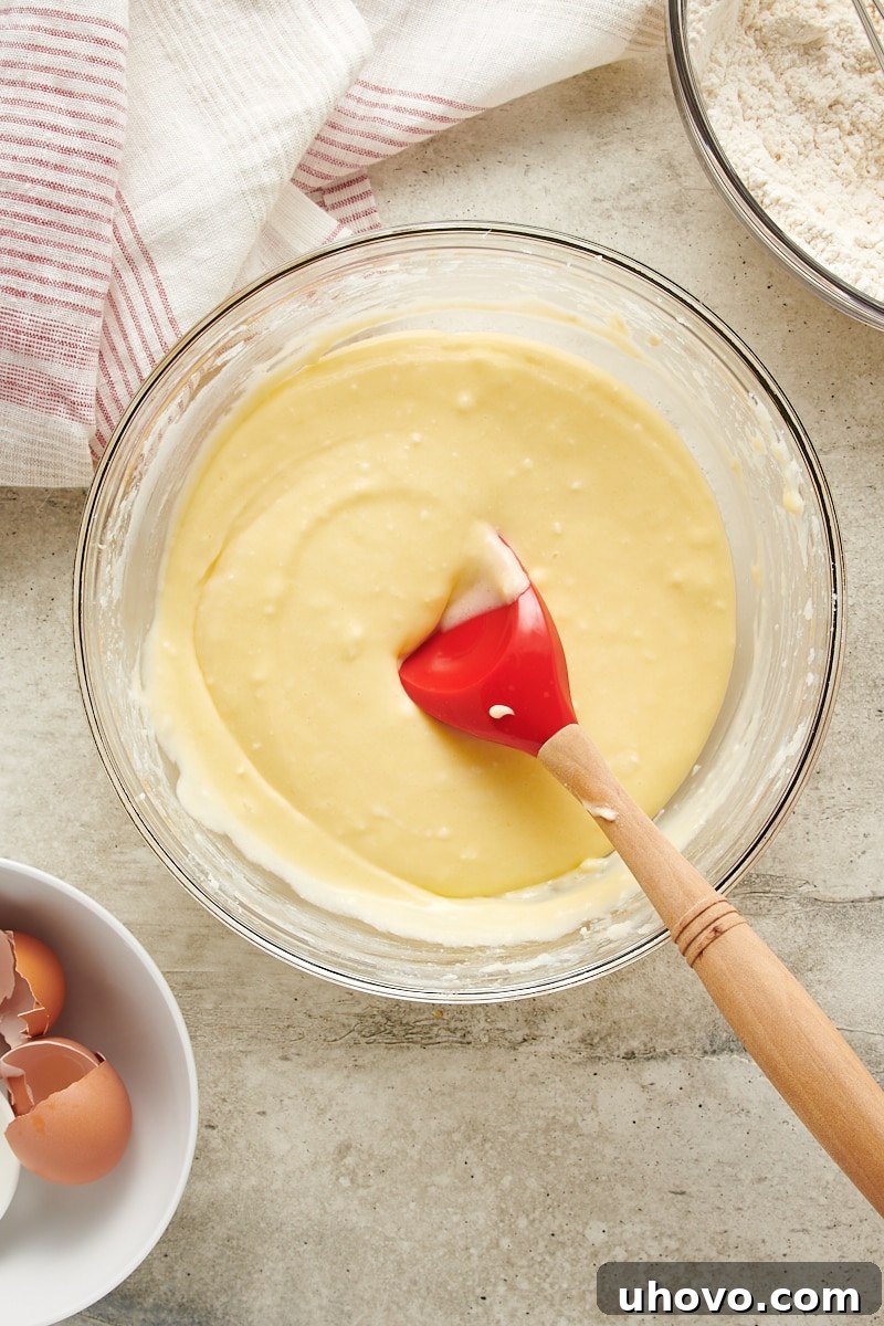 Overhead view of the fluffy, light-colored mixture of butter, cream cheese, and sugar after being creamed, now with eggs and vanilla mixed in, ready for dry ingredients.