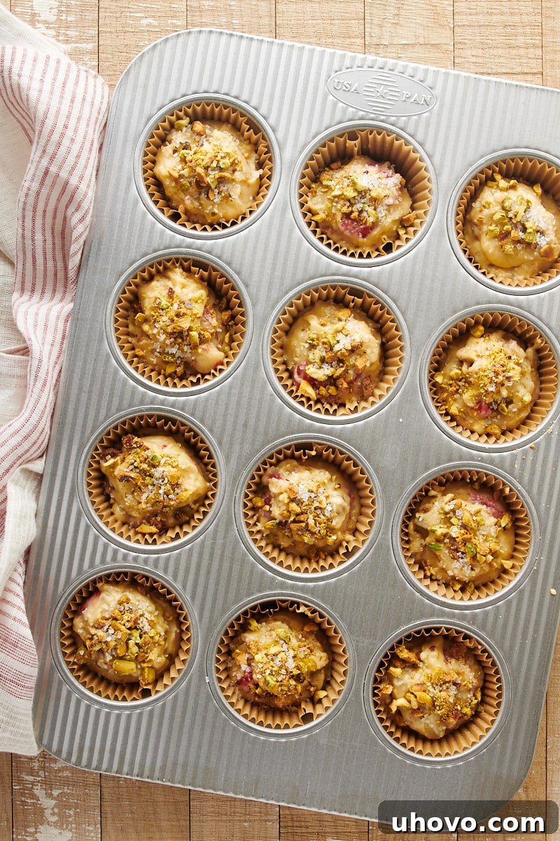 Overhead view of unbaked Raspberry Pistachio Muffin batter neatly portioned into a muffin pan, with a sprinkle of pistachios and sanding sugar on top, ready for the oven.