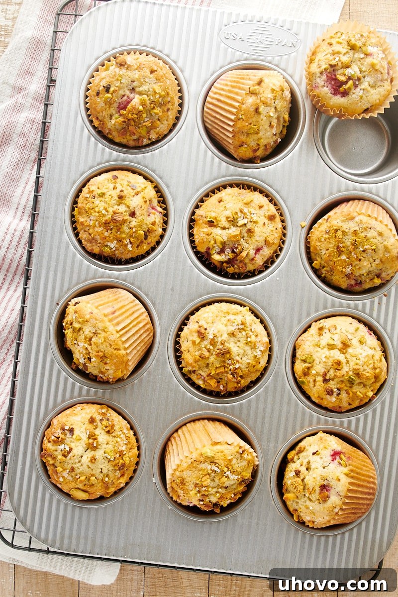 Overhead view of freshly baked Raspberry Pistachio Muffins still in their muffin pan, boasting golden-brown tops and slightly domed appearance, fresh out of the oven.