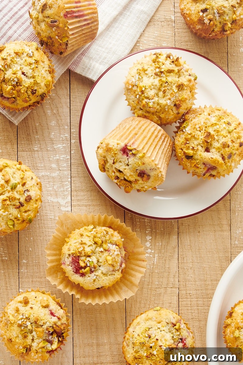 Overhead view of several Raspberry Pistachio Muffins arranged artfully on white plates and directly on a light brown wooden surface, creating an inviting tableau.