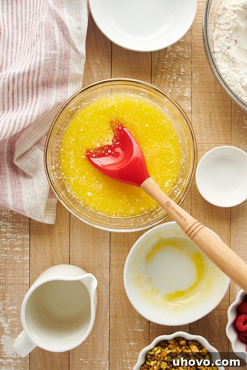 Overhead view of mixed wet ingredients for Raspberry Pistachio Muffins in a glass mixing bowl, showcasing the blended butter, milk, eggs, and almond extract.