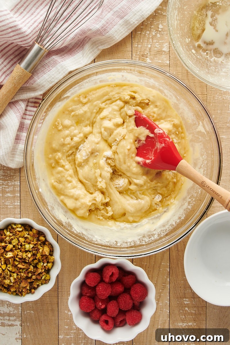 Overhead view of the mixed muffin batter in a glass mixing bowl, showing a slightly lumpy consistency with a few streaks of flour remaining, prior to adding inclusions.