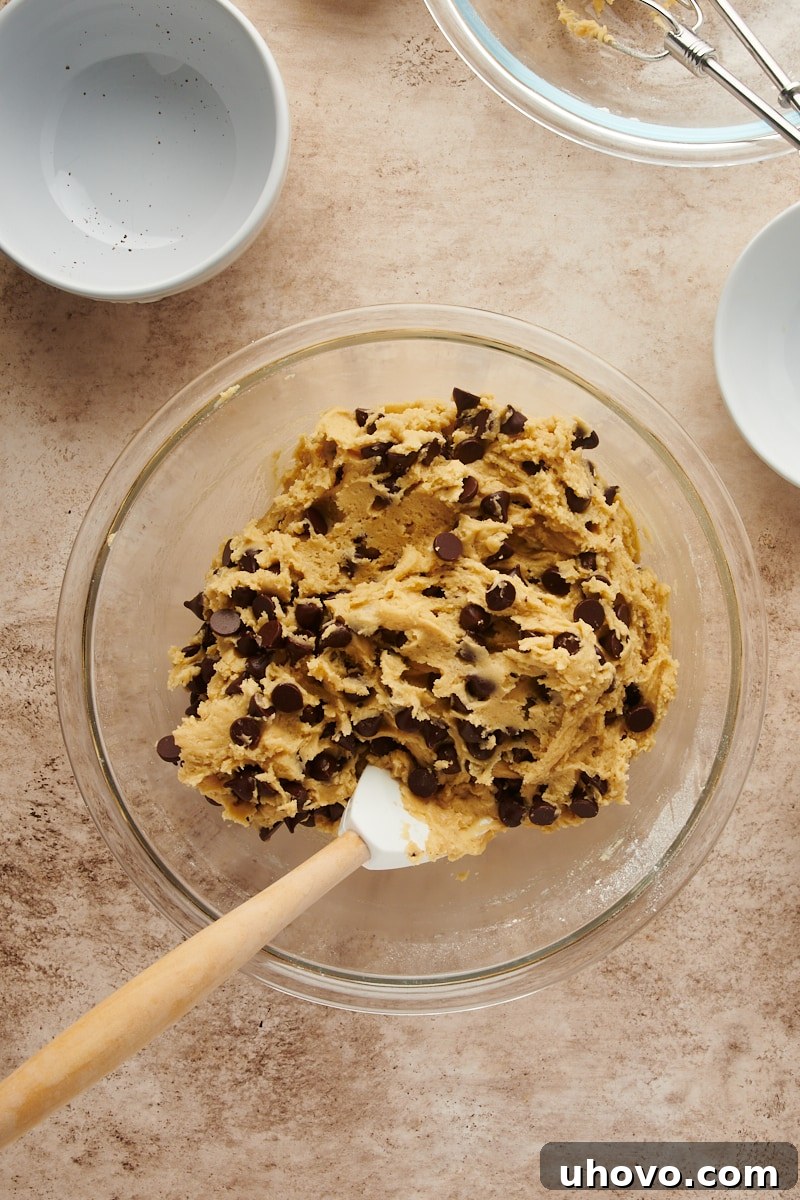 Overhead view of the Cheesecake-Stuffed Chocolate Chip Cookie dough in a glass bowl with semisweet chocolate chips stirred throughout, ready for chilling.