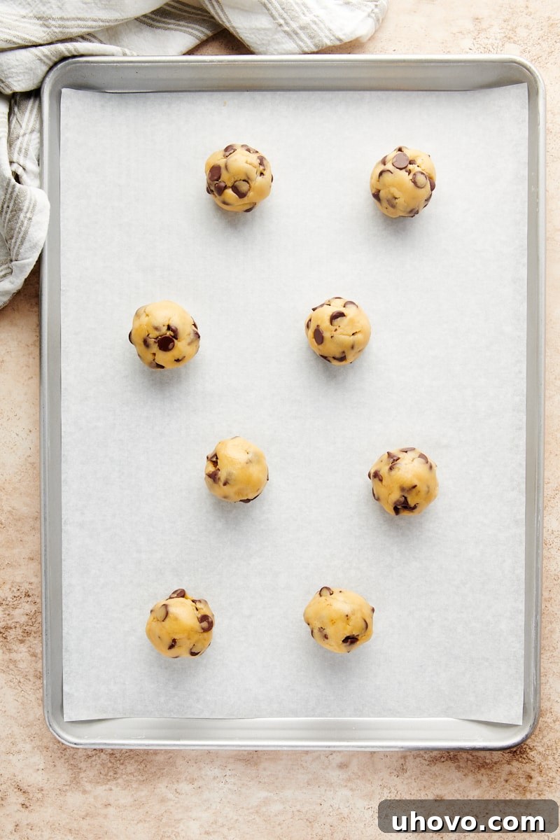 Overhead view of portioned and shaped Cheesecake-Stuffed Chocolate Chip Cookie dough balls neatly arranged on a parchment-lined baking sheet, ready for the oven.