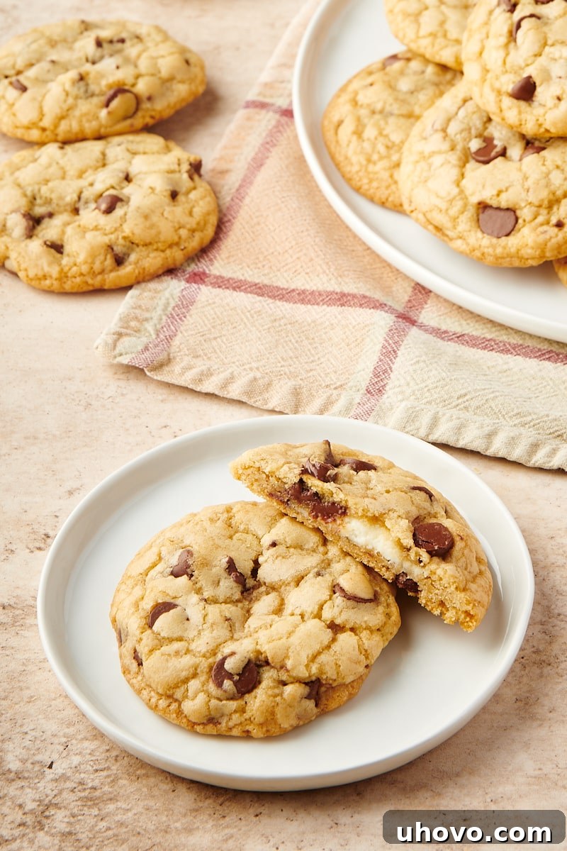 A whole and a half Cheesecake-Stuffed Chocolate Chip Cookie resting on a white plate, with a soft focus on more cookies in the background.