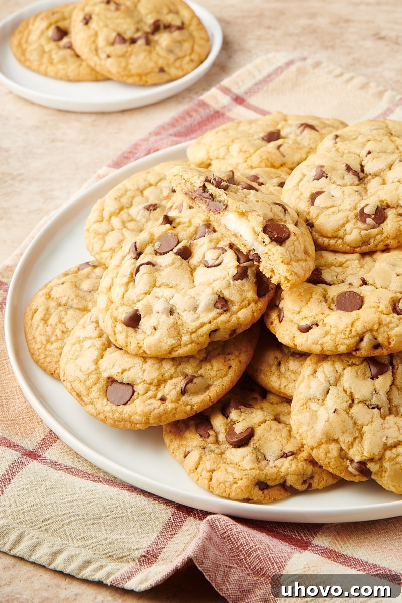 A generous pile of freshly baked Cheesecake-Stuffed Chocolate Chip Cookies arranged on a large white plate, showcasing their inviting texture.