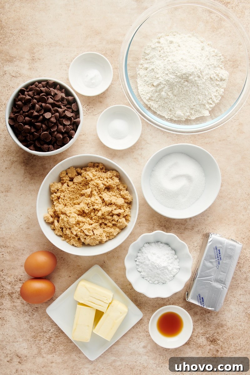 Overhead view of all the measured ingredients neatly laid out for preparing Cheesecake-Stuffed Chocolate Chip Cookies, including flour, sugars, butter, eggs, chocolate chips, and cream cheese.