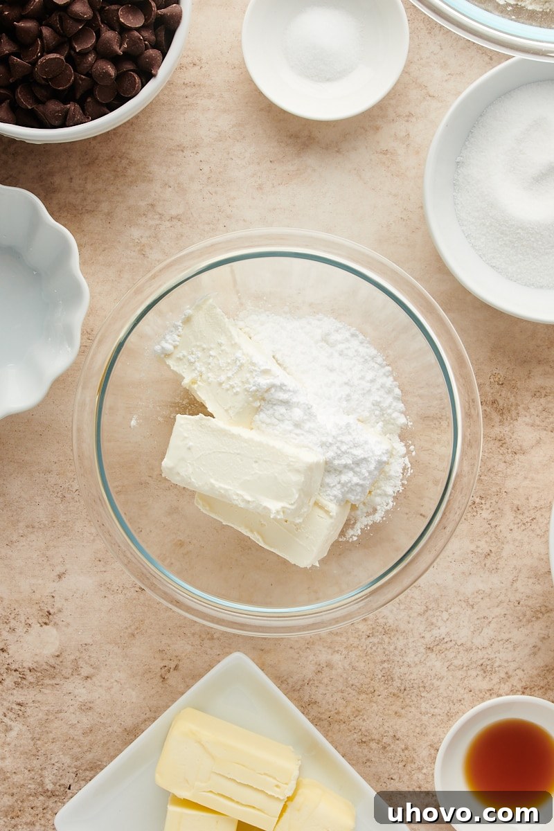 Overhead view of soft cream cheese and white confectioners' sugar in a clear glass mixing bowl, ready to be combined for the filling.