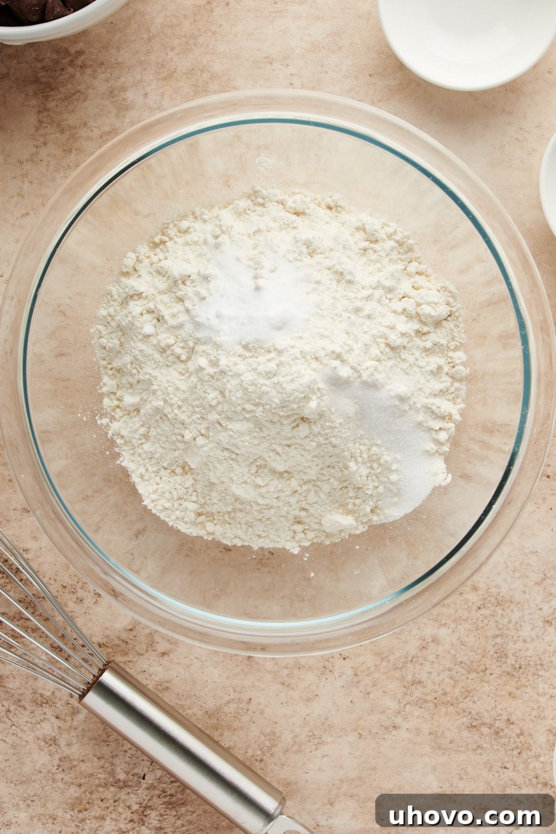 Overhead view of the dry ingredients, including flour, baking soda, and salt, placed together in a glass mixing bowl.