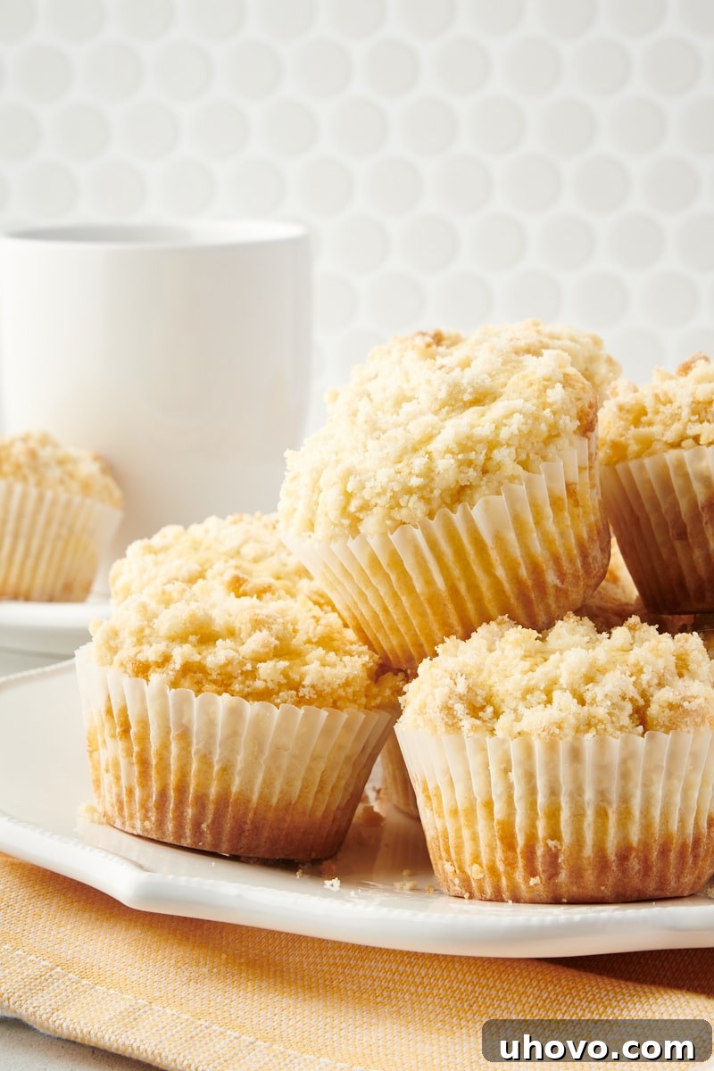 Piled high lemon crumb muffins on a white plate, showcasing their golden tops and generous crumb.