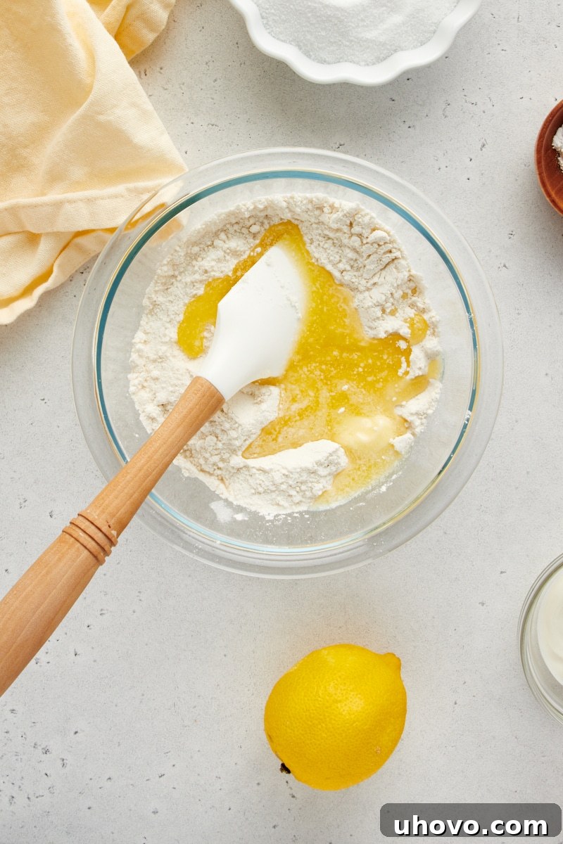 Overhead view of flour, sugar, and salt in a glass mixing bowl with melted butter being poured in.