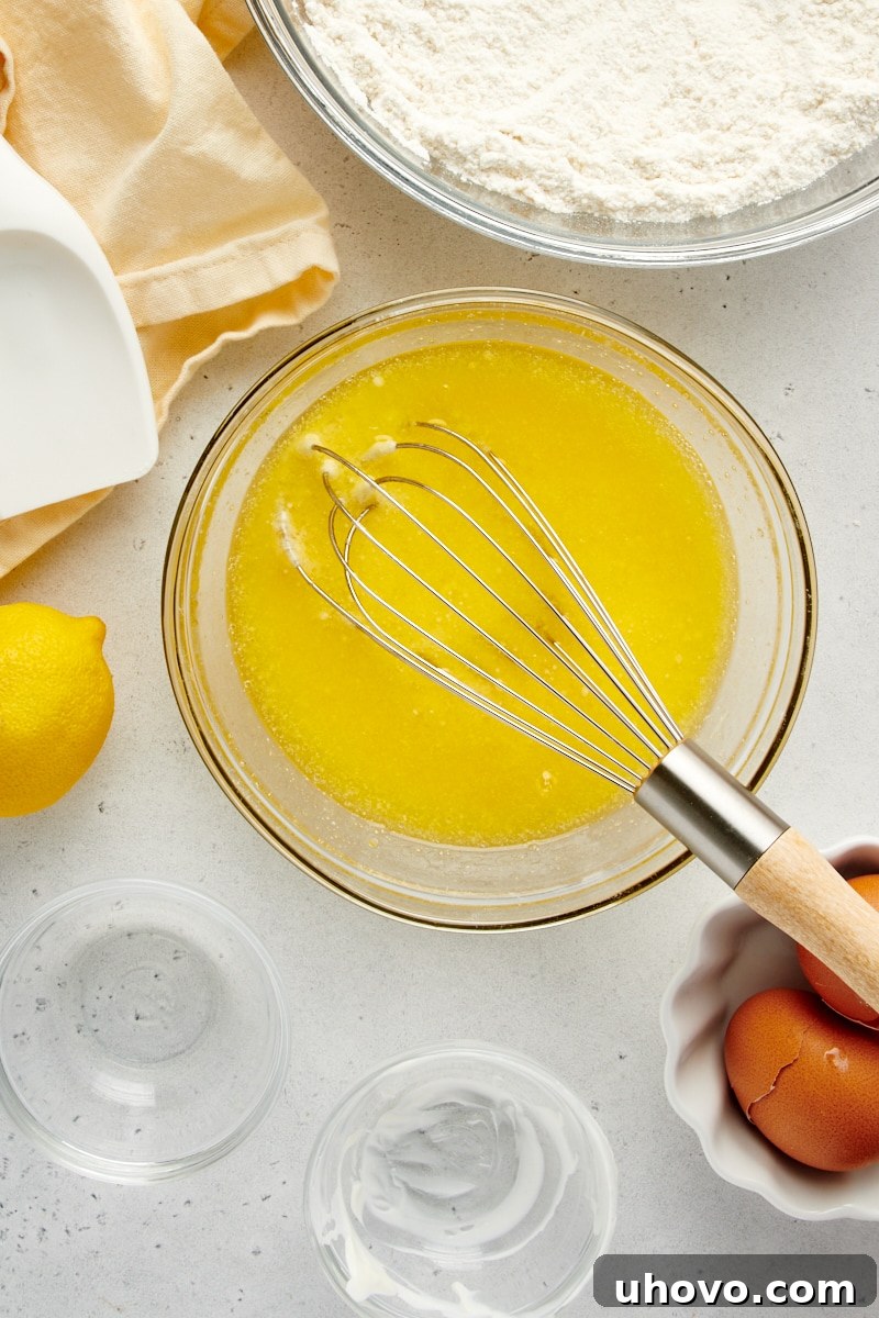 Overhead view of thoroughly mixed wet ingredients, including cooled butter, sour cream, milk, eggs, and lemon juice, in a glass mixing bowl.