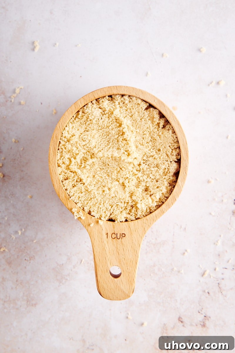 Close-up overhead view of light brown sugar in a wooden measuring cup, with a rustic wooden background.