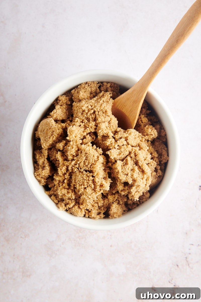 Close-up overhead view of dark brown sugar in a white bowl, contrasting against a light background.