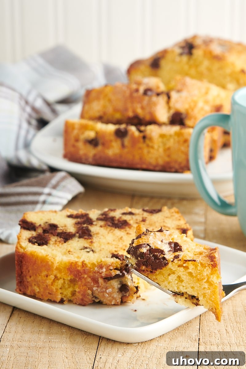 A delectable slice of Chocolate Chip Loaf Cake on a white plate with a bite taken from a fork, emphasizing its soft and moist texture