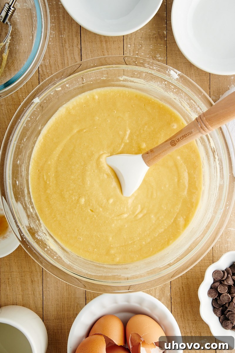 Cake batter for Chocolate Chip Loaf Cake in a mixing bowl, showing the process of alternating dry ingredients and milk being mixed in