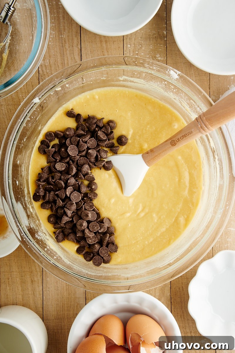 Overhead view of chocolate chips being added to the cake batter in a clear glass mixing bowl