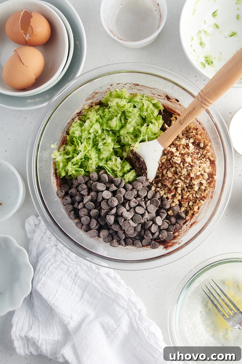 An overhead view of grated zucchini, chocolate chips, and chopped nuts being added to the quick bread batter.