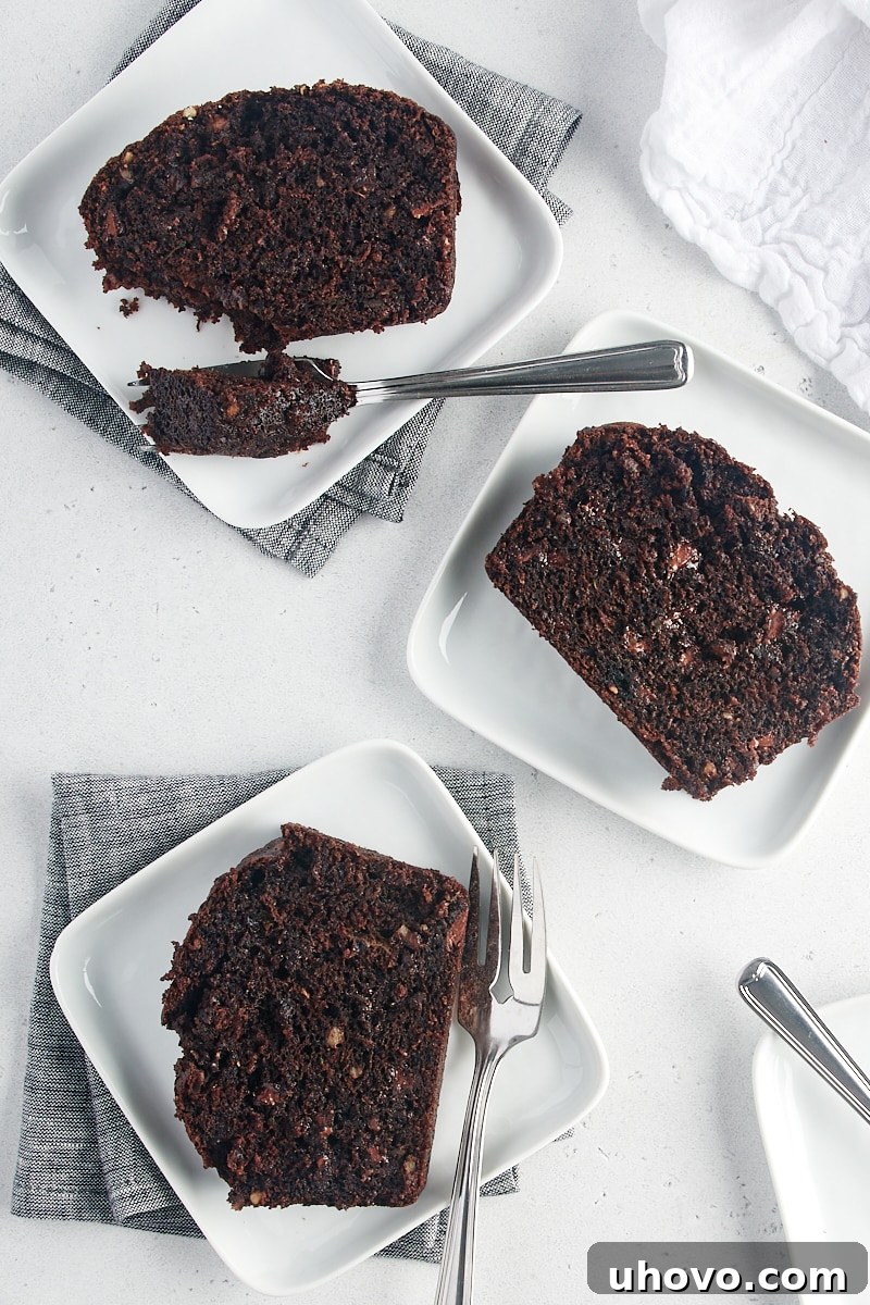 An overhead view of several slices of Chocolate Zucchini Bread arranged on white plates, highlighting the bread's moist interior and chocolate chips.