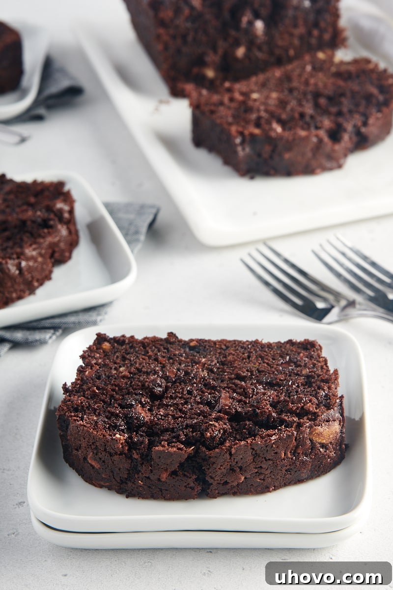 A slice of Chocolate Zucchini Bread on a white plate, with more servings visible in the background.