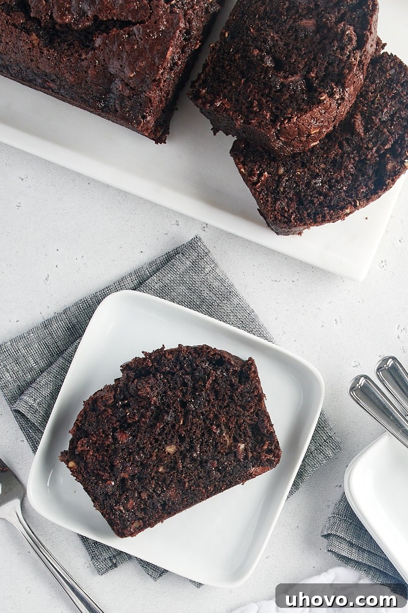 A single slice of rich Chocolate Zucchini Bread rests on a white plate, showcasing its moist texture and chocolate chips.