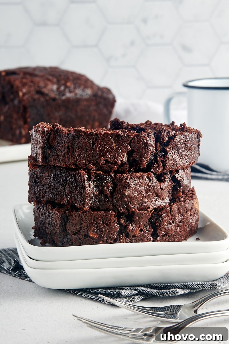 Multiple slices of moist Chocolate Zucchini Bread stacked neatly on a white plate.