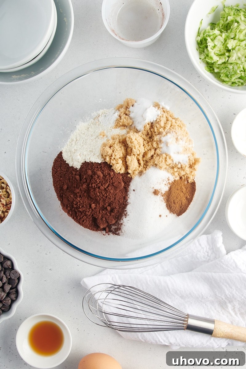 An overhead view of flour, sugars, cocoa powder, baking powder, baking soda, cinnamon, and salt in a glass mixing bowl.