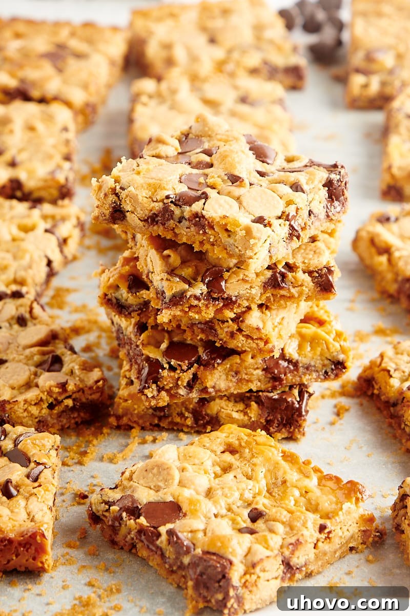 Stack of perfectly cut Double Delicious Cookie Bars on parchment paper, showcasing their thick, chewy layers of chocolate and peanut butter.