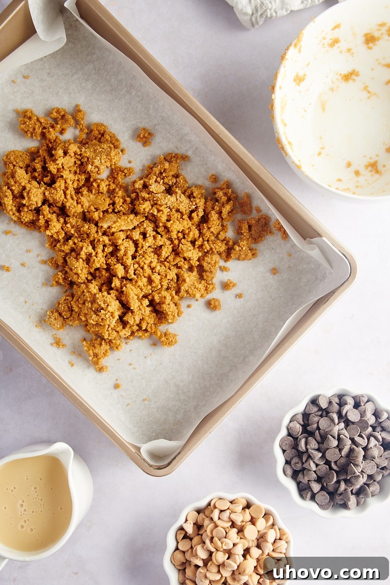 Overhead view of graham cracker crumbs being added evenly to the prepared baking pan, starting the crust formation.