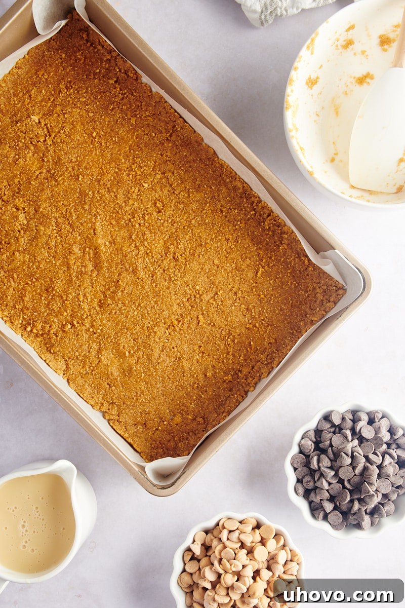 Overhead view of the compacted graham cracker crust pressed evenly into the bottom of the baking pan, forming a solid base.
