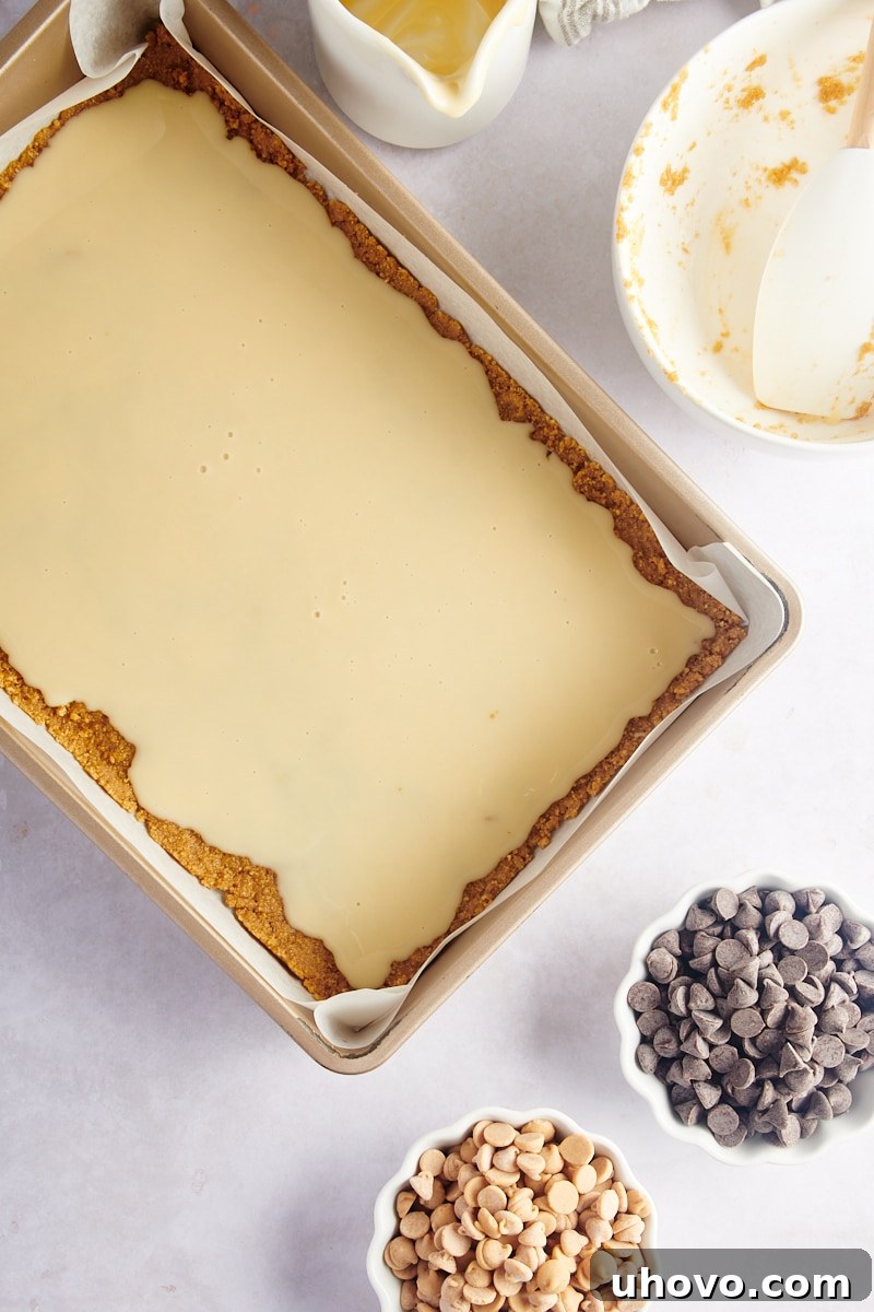 Overhead view of the graham cracker crust in the pan, topped with a layer of sweetened condensed milk, before adding the chocolate and peanut butter chips.