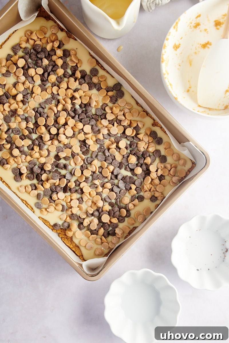 Overhead view of the fully assembled cookie bars in the pan, featuring the graham cracker crust, condensed milk, and a generous topping of chocolate and peanut butter chips, ready for baking.