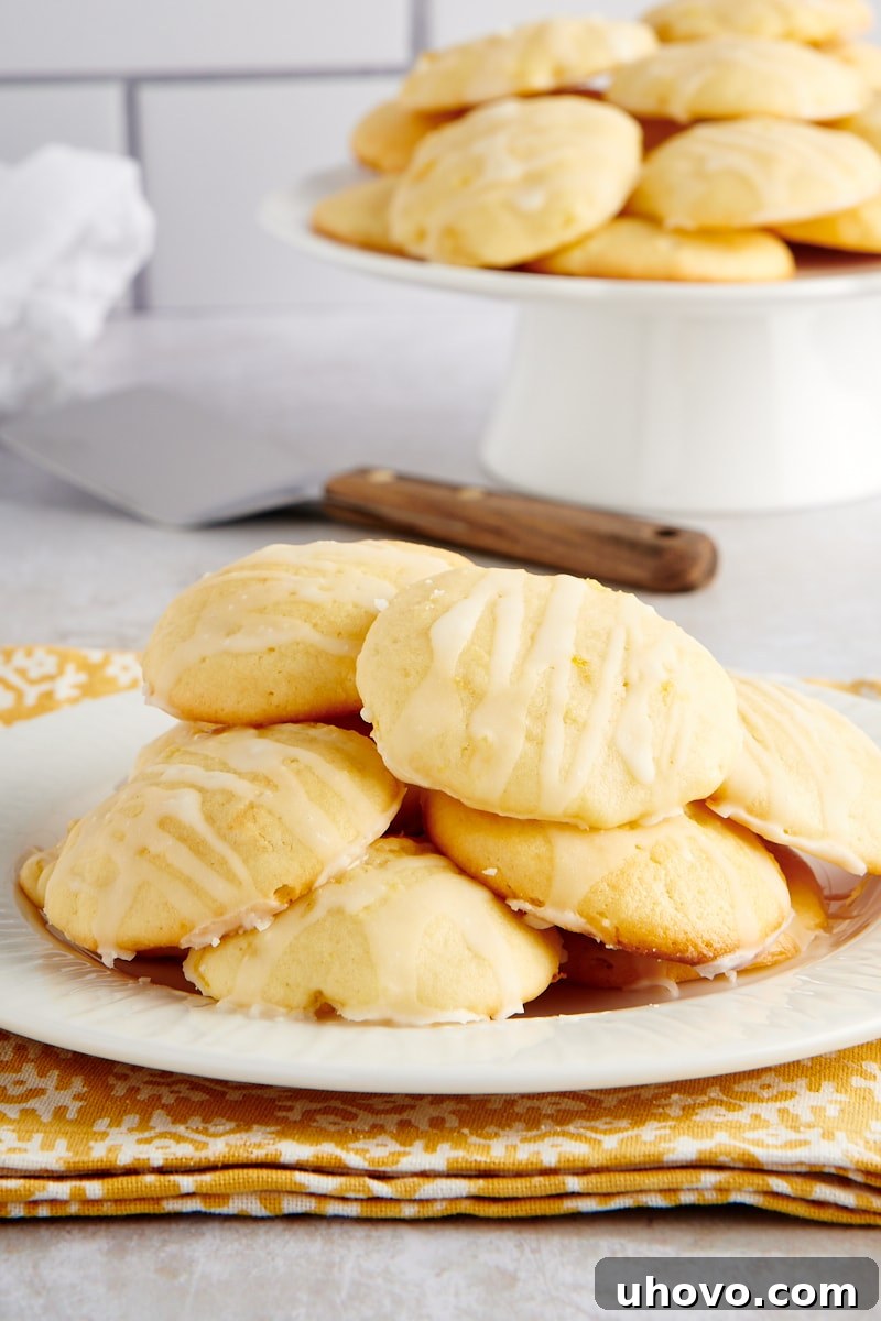Pile of soft Pineapple Cream Cheese Cookies with a glistening glaze on a white plate, with more cookies in the background