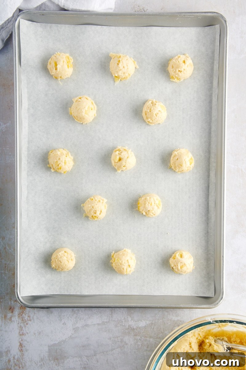 Overhead view of perfectly scooped Pineapple Cream Cheese Cookie dough portions arranged on a parchment-lined baking sheet, ready for the oven