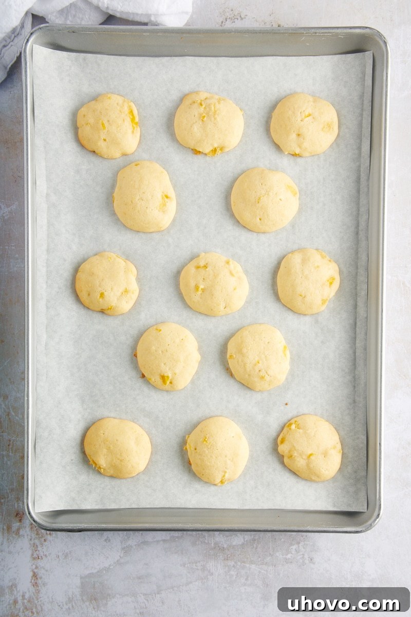 Overhead view of freshly baked Pineapple Cream Cheese Cookies cooling on a parchment-lined baking sheet, golden brown at the edges and perfectly puffed