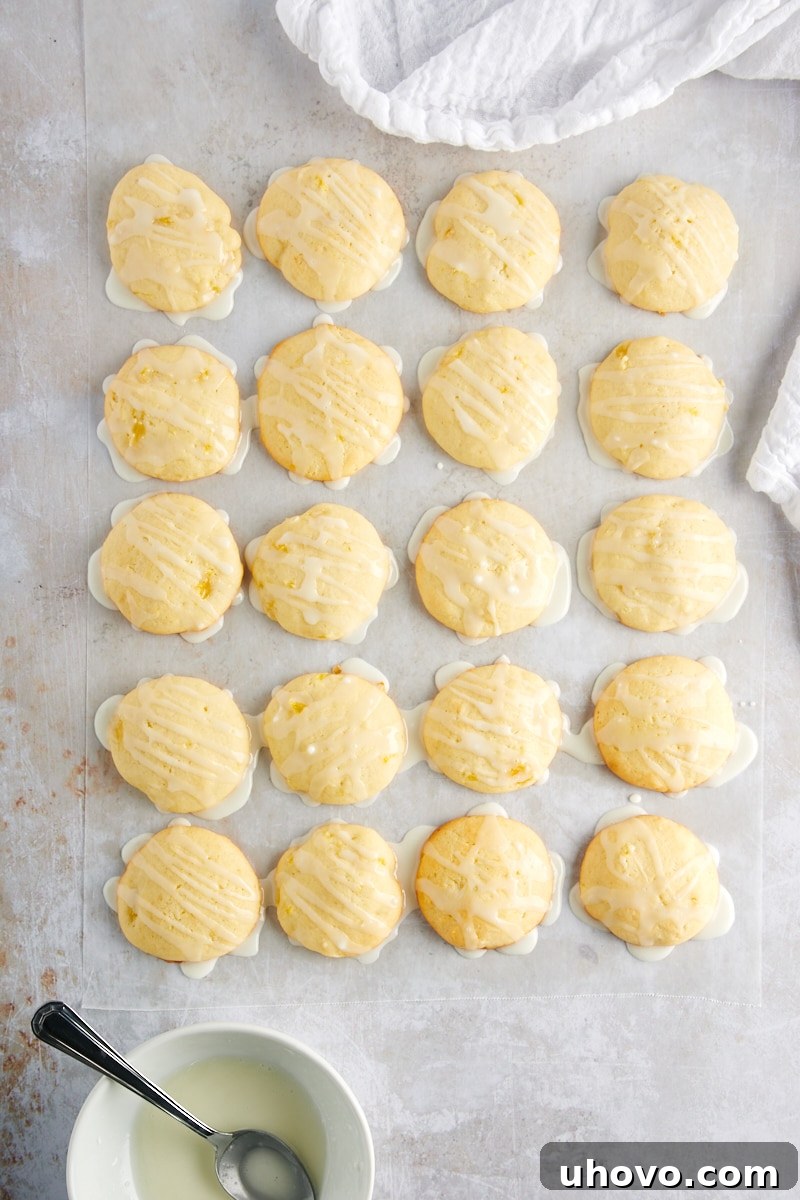 Overhead view of freshly glazed Pineapple Cream Cheese Cookies neatly arranged on waxed paper, with the sweet drizzle glistening