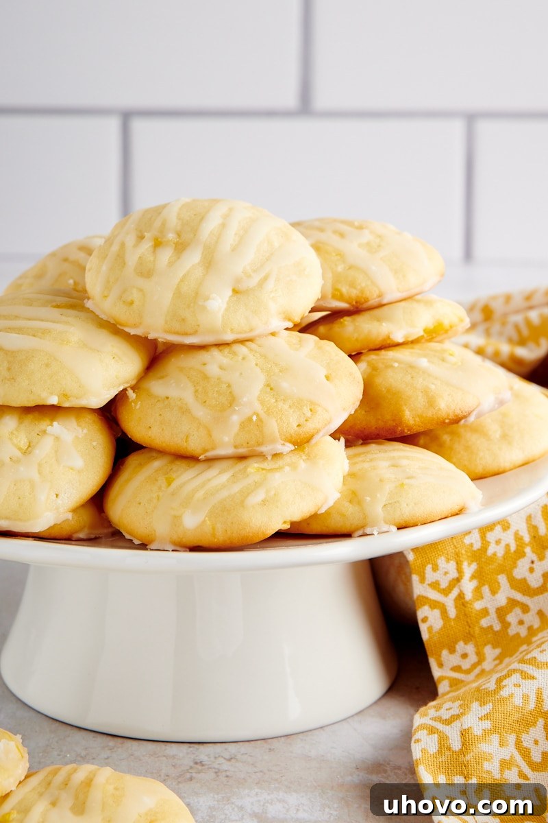 Pineapple Cream Cheese Cookies neatly piled on a small, elegant white cake stand, showcasing their soft texture and delicate glaze